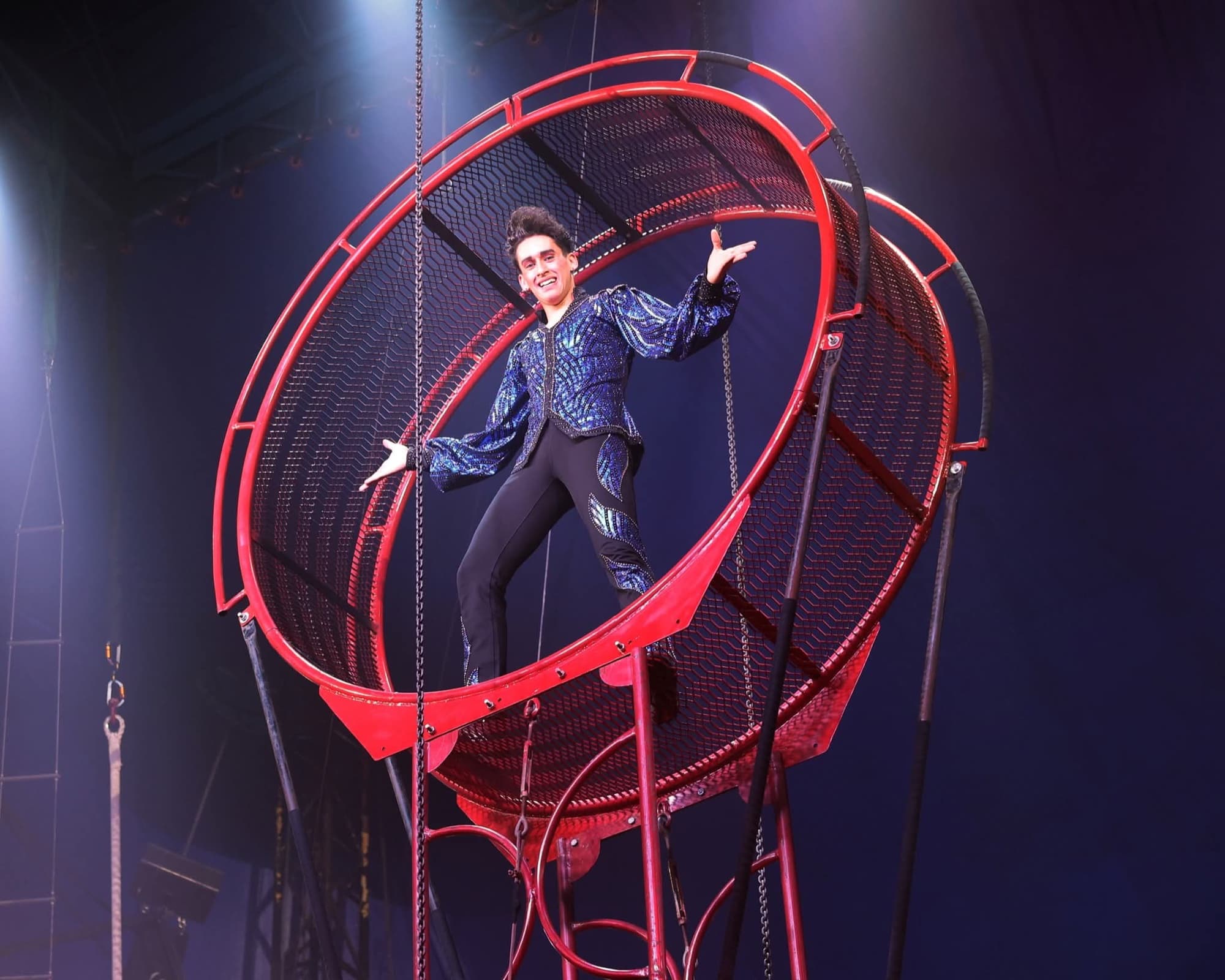 A performer standing inside the Wheel of Destiny, a giant rotating steel wheel, high above the floor
