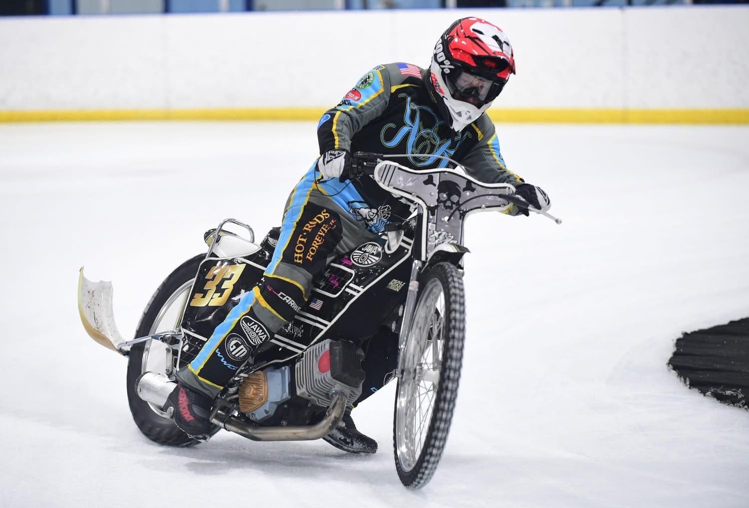A speedway bike sliding through a corner on arena ice, the rider's left foot out